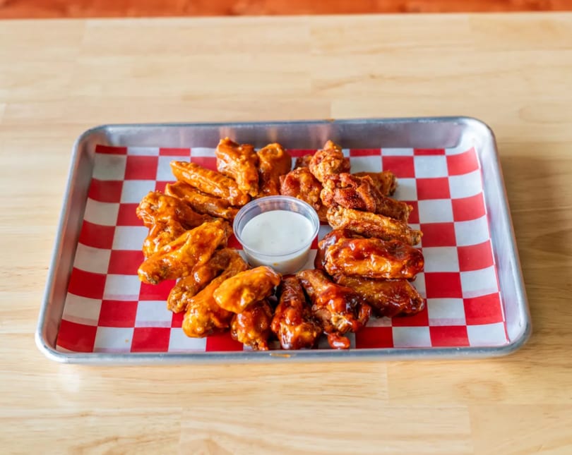 A metal tray of chicken wings in various sauces with a side of ranch dressing.