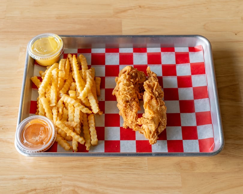 Crispy chicken tenders and crinkle-cut fries with two dipping sauces on a checkered tray.