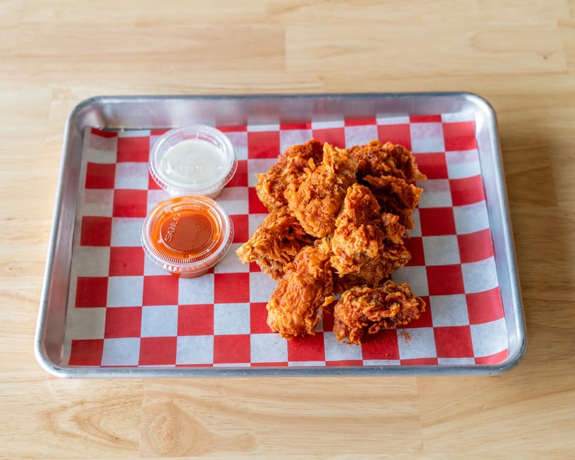 Crispy fried chicken pieces with two dipping sauces on a red and white checkered paper-lined tray.
